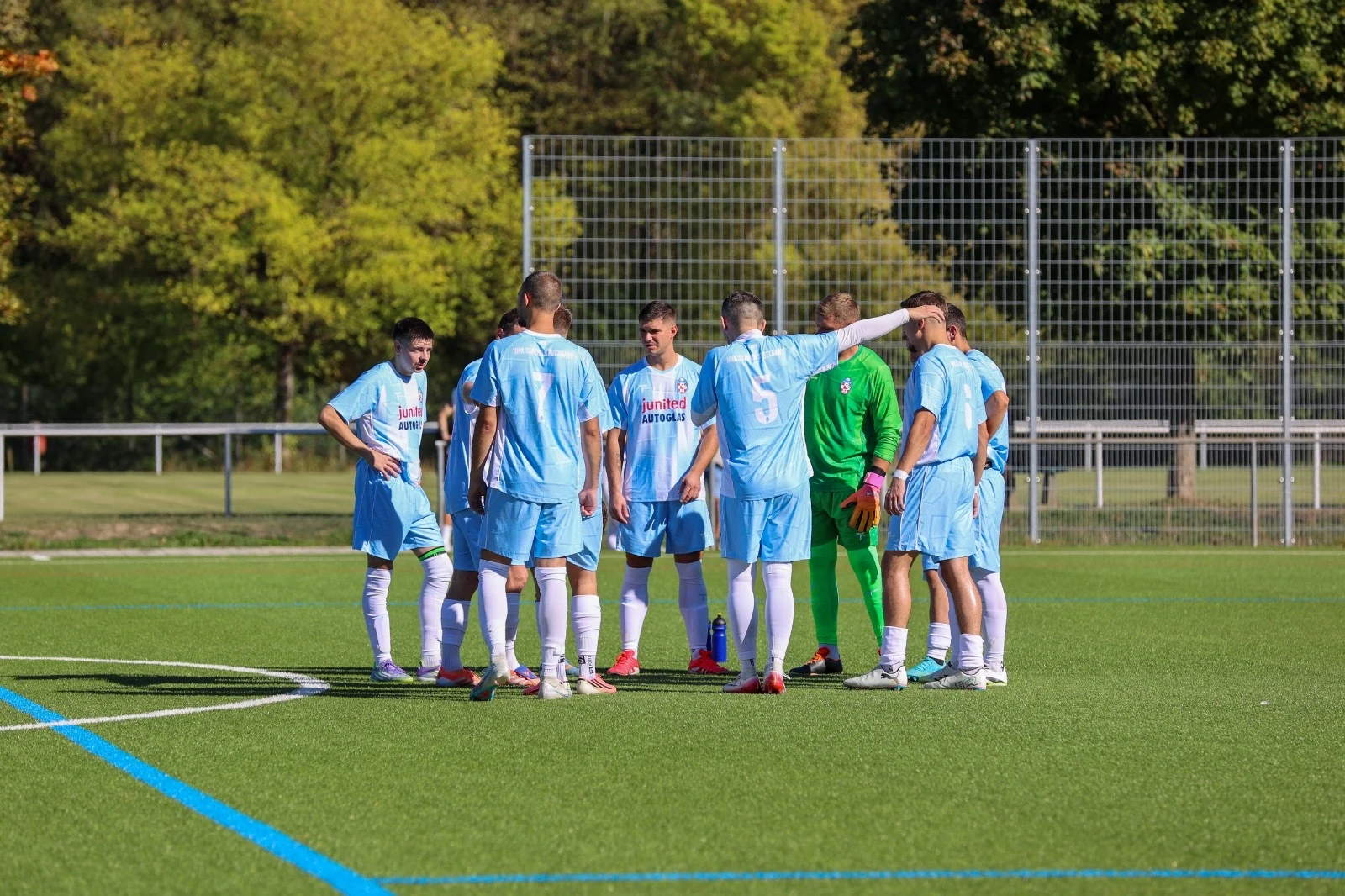 Mannschaft im Kreis auf dem Fußballplatz, hellblaue Trikots.
