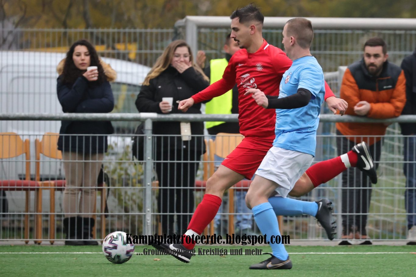 Zwei Fußballspieler im Wettkampf, Zuschauer im Hintergrund.