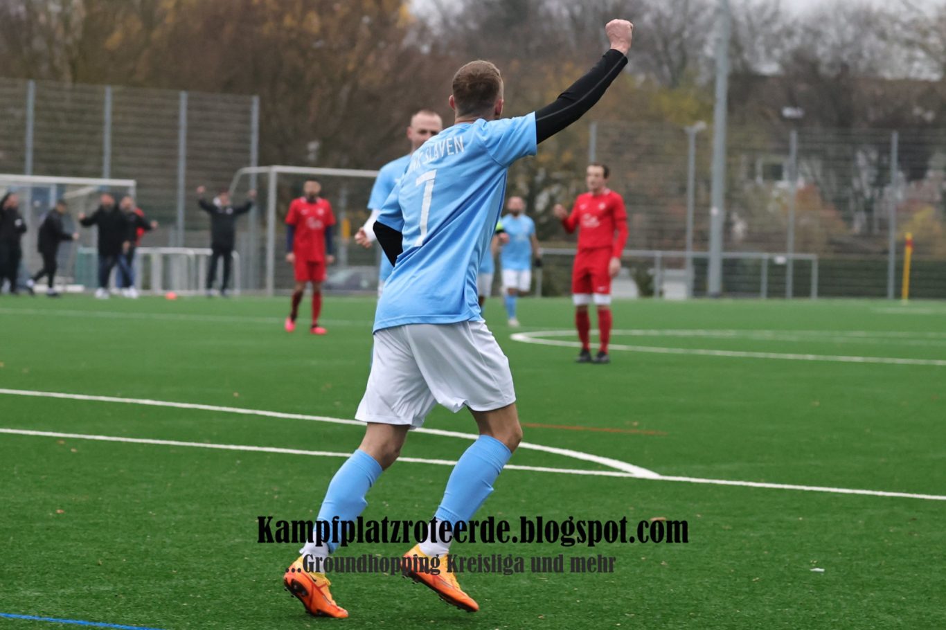 Ein Fußballspieler in hellblauem Trikot jubelt nach einem Tor, im Hintergrund Spieler in Rot.