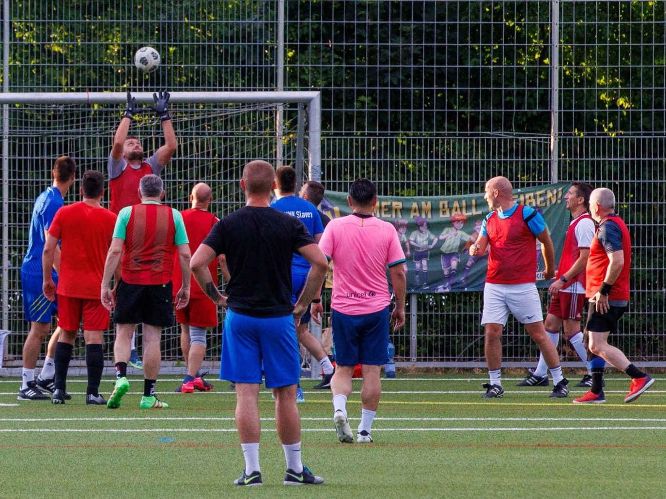 Fußballspiel mit Spielern in rot und blau auf einem Kunstrasenplatz.