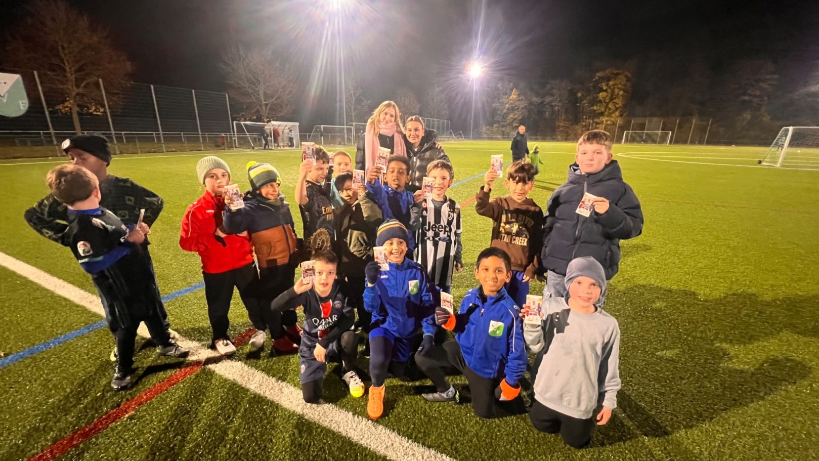 Gruppe von Kindern in Sportkleidung auf einem Fußballfeld bei Nacht.
