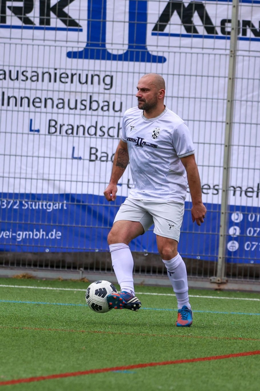 Ein Fußballspieler in weißem Trikot steht auf dem Feld und bereitet sich auf einen Pass vor.