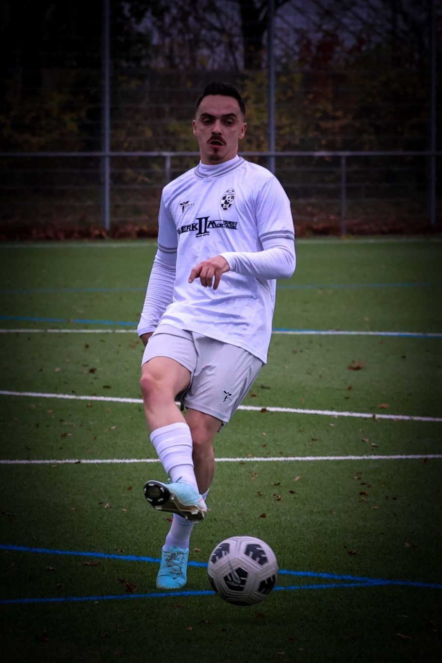 Ein Fußballspieler führt einen Schuss auf einem grünen Platz aus.