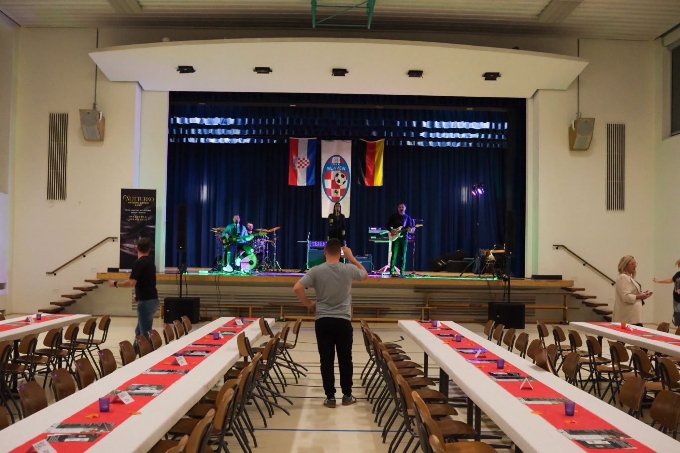 Bühne mit Band, Tischen im Saal, Fahnen im Hintergrund, Teilnehmer am Tanzen.