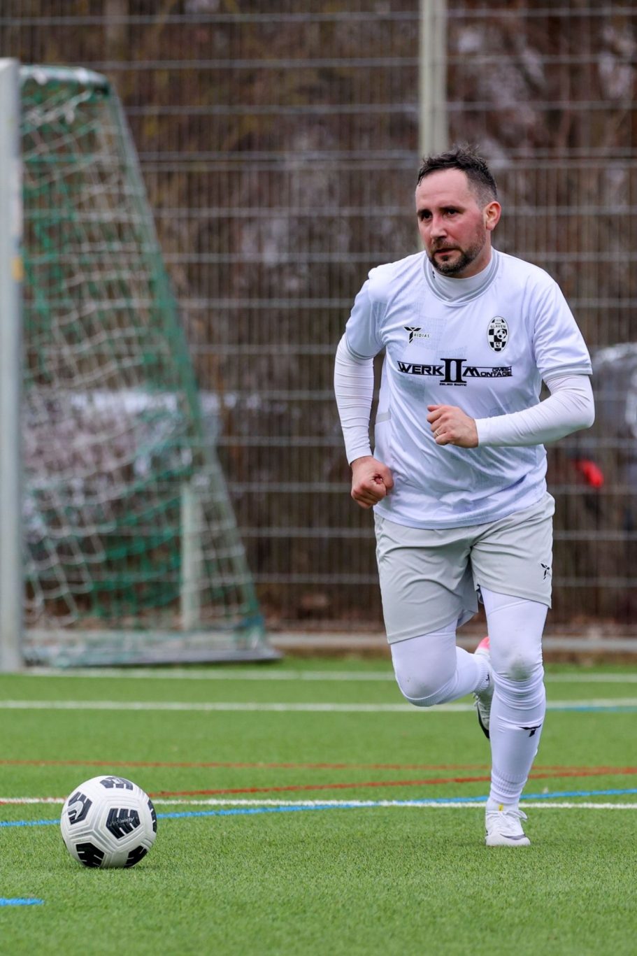 Fußballspieler in weißem Trikot läuft mit Ball auf dem Spielfeld.